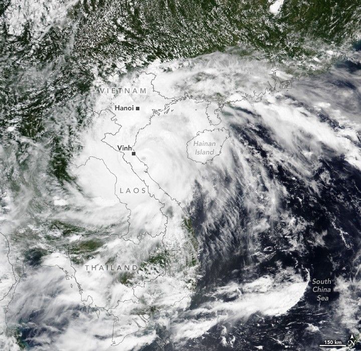 swirling clouds obscure Vietnam, Laos, and Hainan Island from view completely as well as most of Thailand. The countries borders are superimposed over the cloud with the their names and the cities of Hanoi and Vinh labeled. The South China Sea's deep blue waters are visible in the lower right, and what land is visible appears covered with foliage.