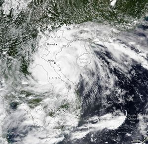 swirling clouds obscure Vietnam, Laos, and Hainan Island from view completely as well as most of Thailand. The countries borders are superimposed over the cloud with the their names and the cities of Hanoi and Vinh labeled. The South China Sea's deep blue waters are visible in the lower right, and what land is visible appears covered with foliage.