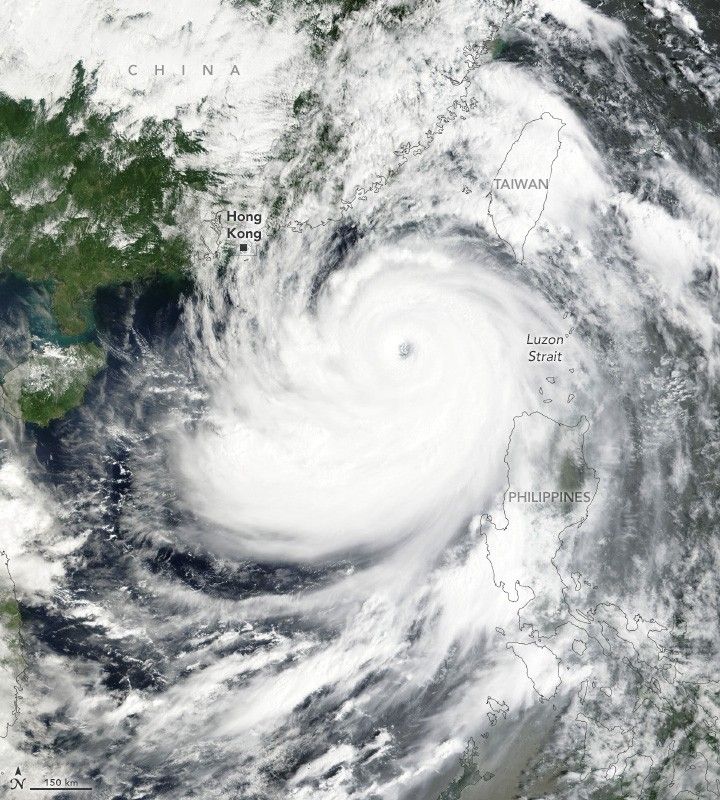 Swirling white clouds off the coast of China, also mostly covered by clouds with some green foliage covered landscape visible. Taiwan and the Philippines are both completely obscured by clouds, but the island outlines are overlaid on the image.
