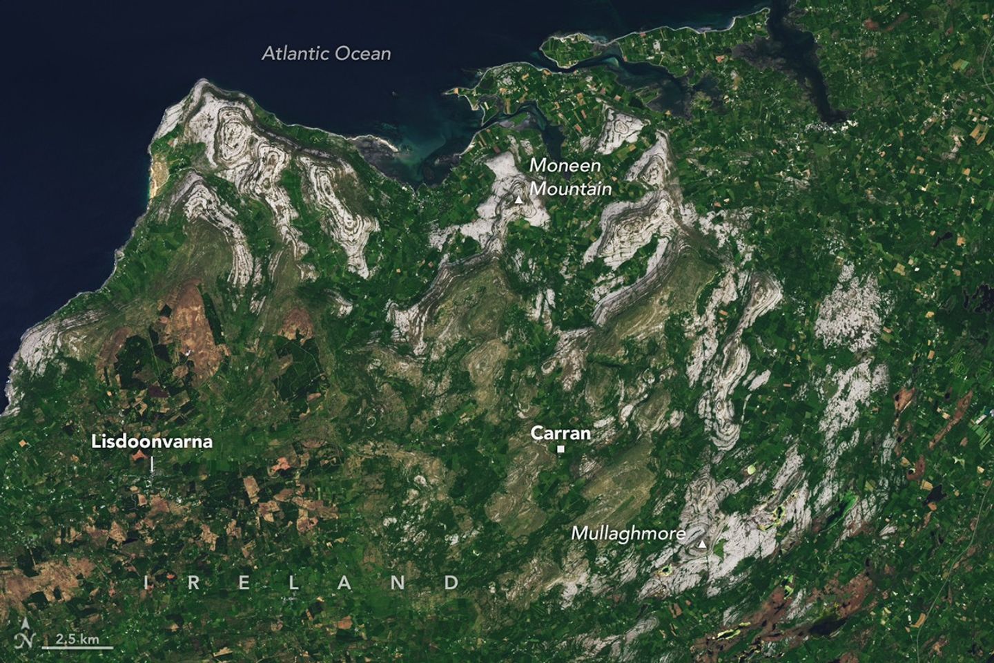 A satellite view of the Burren in western Ireland shows gray limestone hills arranged in curved, concentric bands surrounded by green farmland and small towns.
