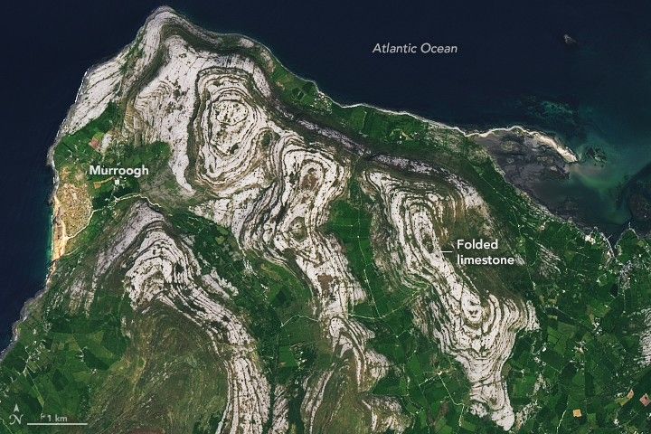 A detailed view of folded limestone in the Burren. The limestone forms swirling, layered patterns of gray rock separated by thin green bands of vegetation.