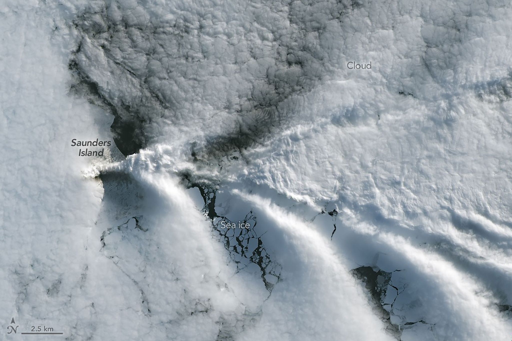 A series of V-shaped wave clouds appears over an ocean filled with pieces of sea ice.