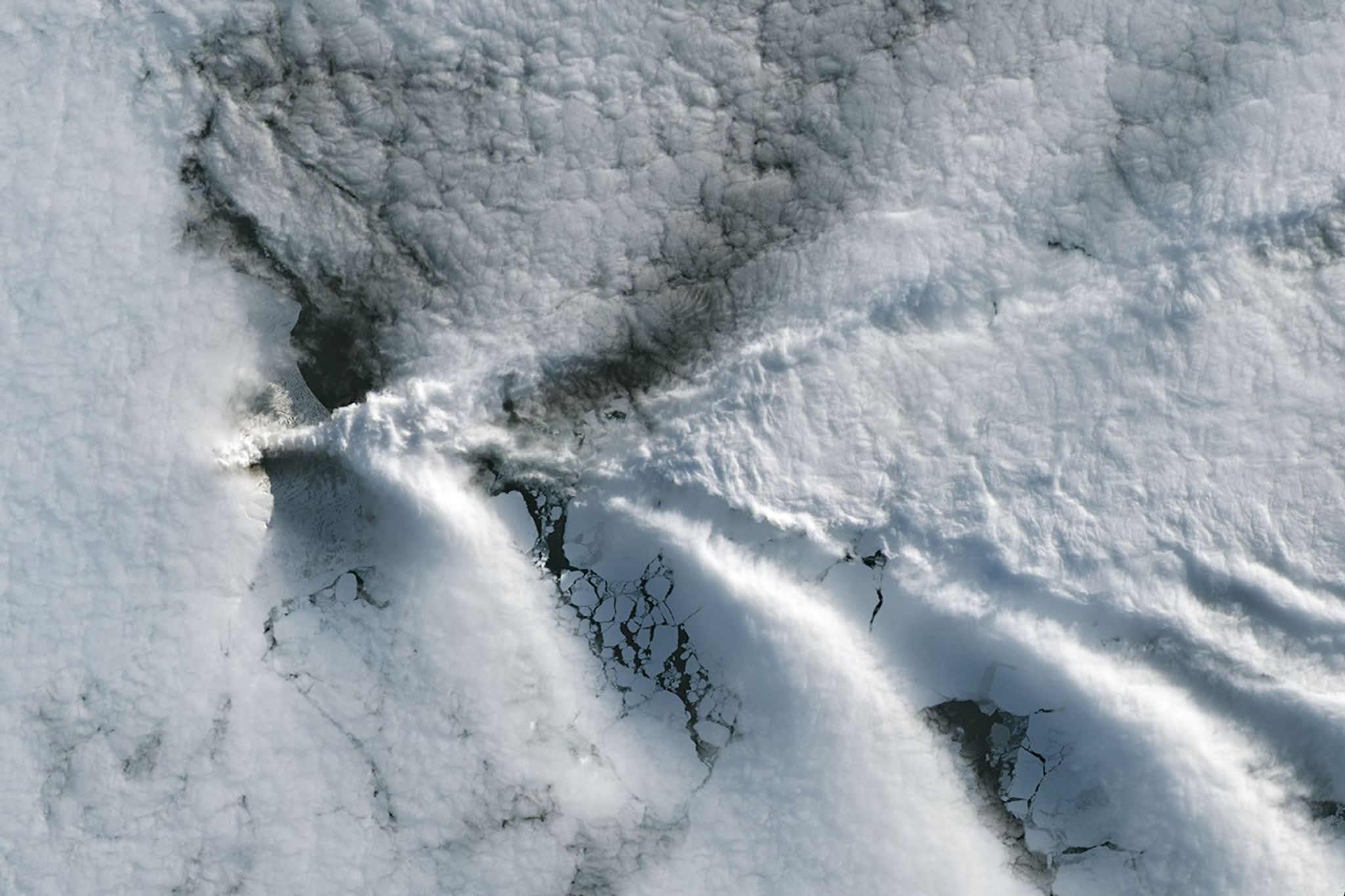 A series of V-shaped wave clouds appears over an ocean filled with pieces of sea ice.