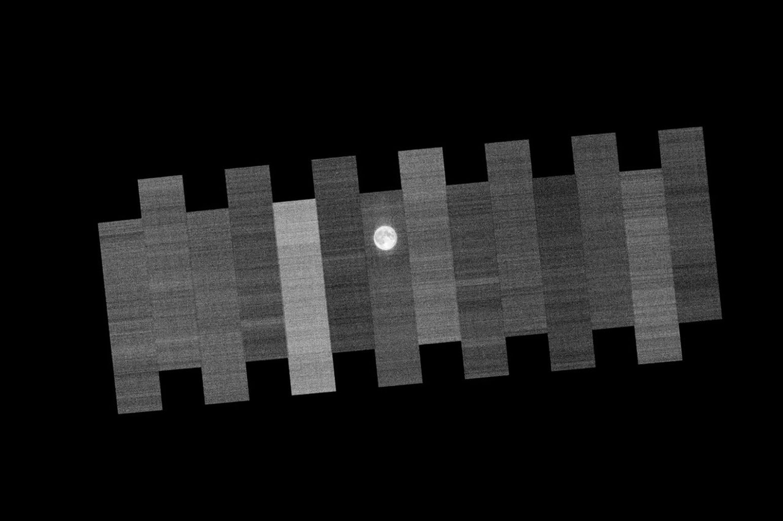 Franjas de escaneo paralelas en escala de grises del Landsat 9, con la Luna apareciendo cerca de la línea central de franjas alternas antes de aparecer finalmente en todas las franjas.