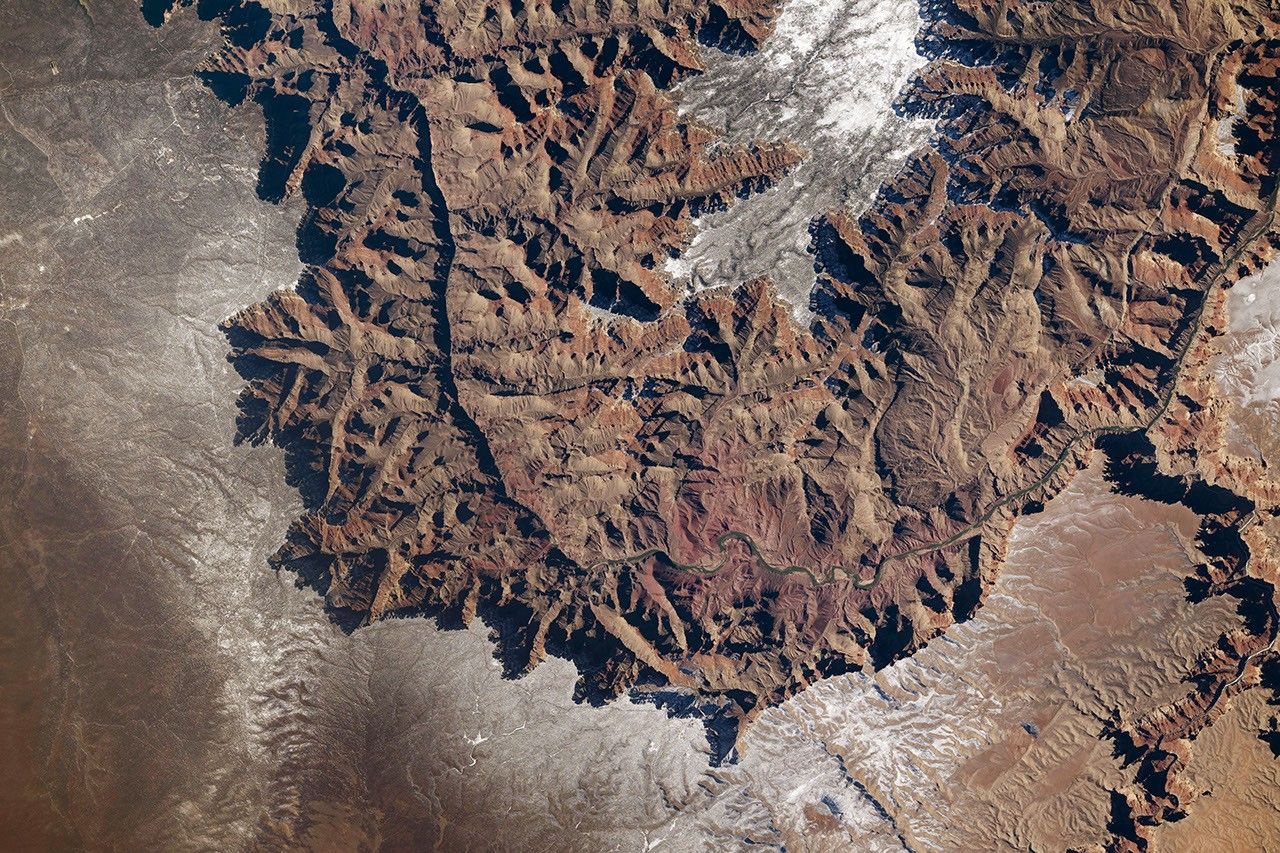 A portion of the Grand Canyon, photographed from above, forms a U shape. The plateau on both sides of the canyon is partially covered in a layer of white snow.