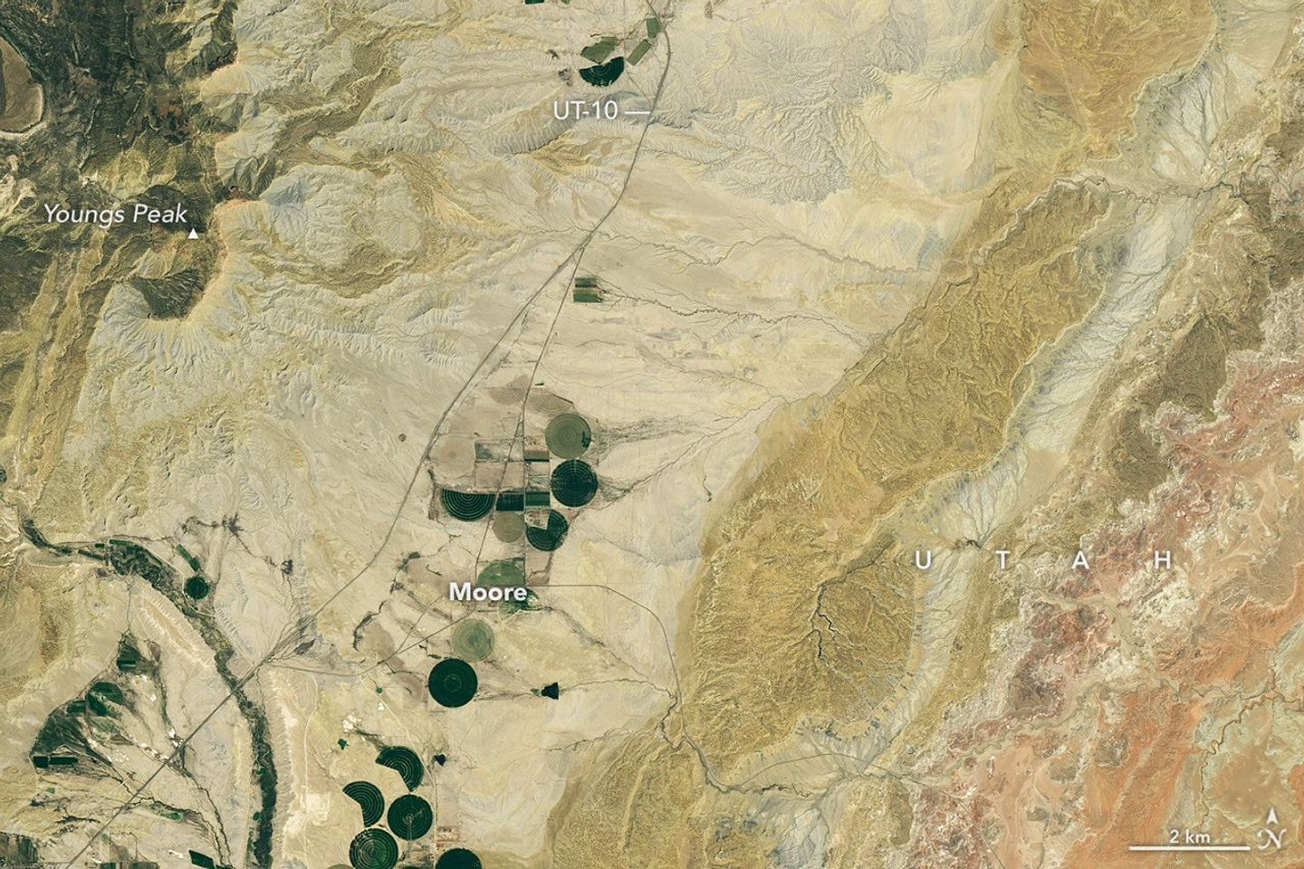 A dry, tan-colored valley containing a few circular irrigated fields runs roughly north-south through the image.