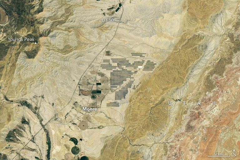 Grid-like arrays of solar panels cover parts of a valley floor in a brown, dry-looking area of Utah.