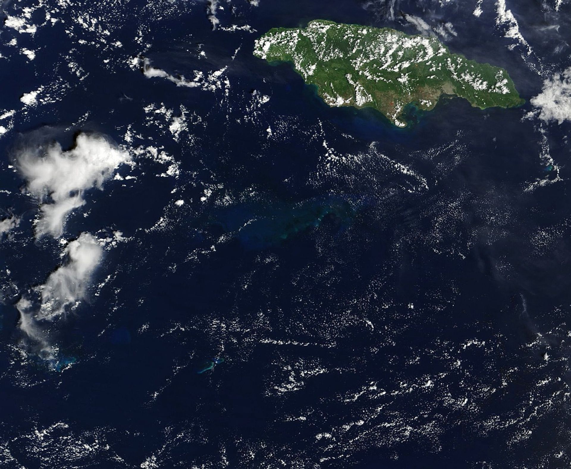 A satellite view of part of the Caribbean Sea shows Jamaica in the upper right and light blue waters over a submerged carbonate platform in the center.