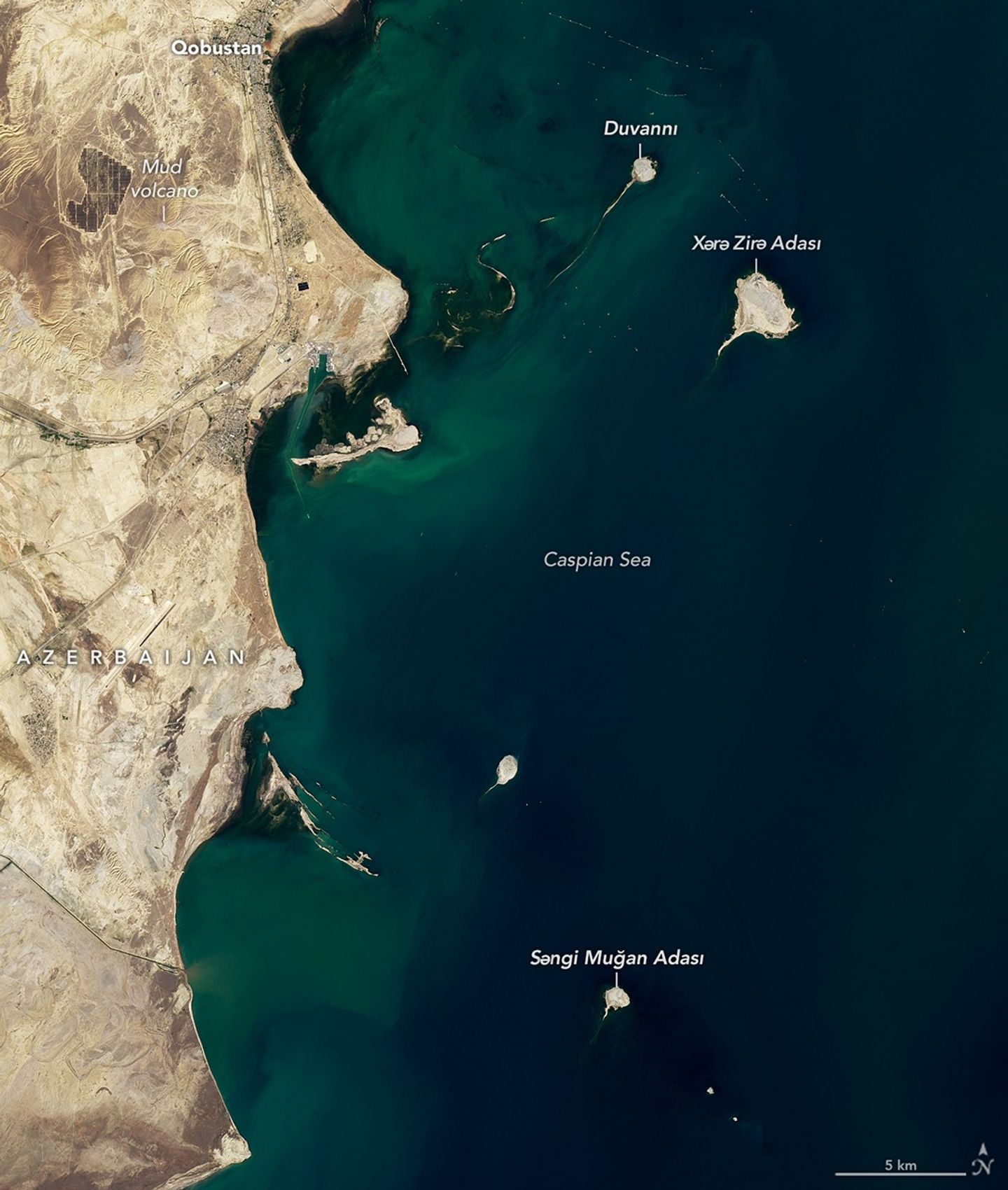 Satellite view of a tadpole-shaped brown land area encircled by blue-green water.