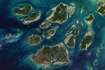 A satellite image shows a cluster of green islands surrounded by beige sand flats and networks of channels full of dark blue water.