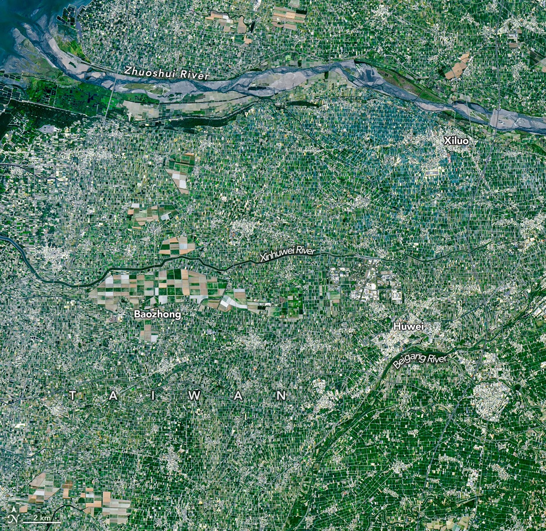 An array of green rectangular parcels of farmland in a range of hues is interspersed with several small towns.