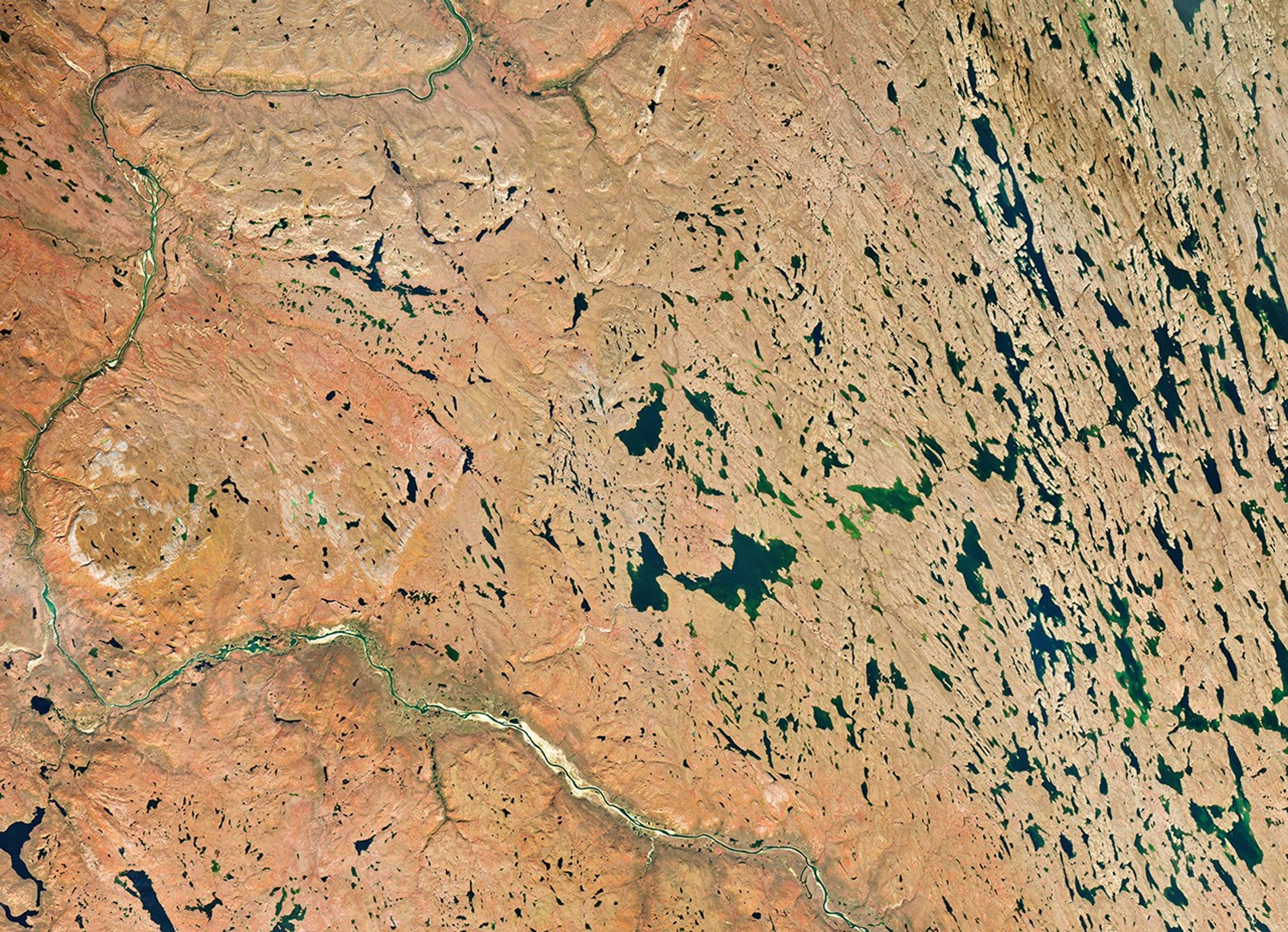 A river winds through the same tundra landscape in autumn, now colored red and orange. Some green vegetation remains visible along the river.