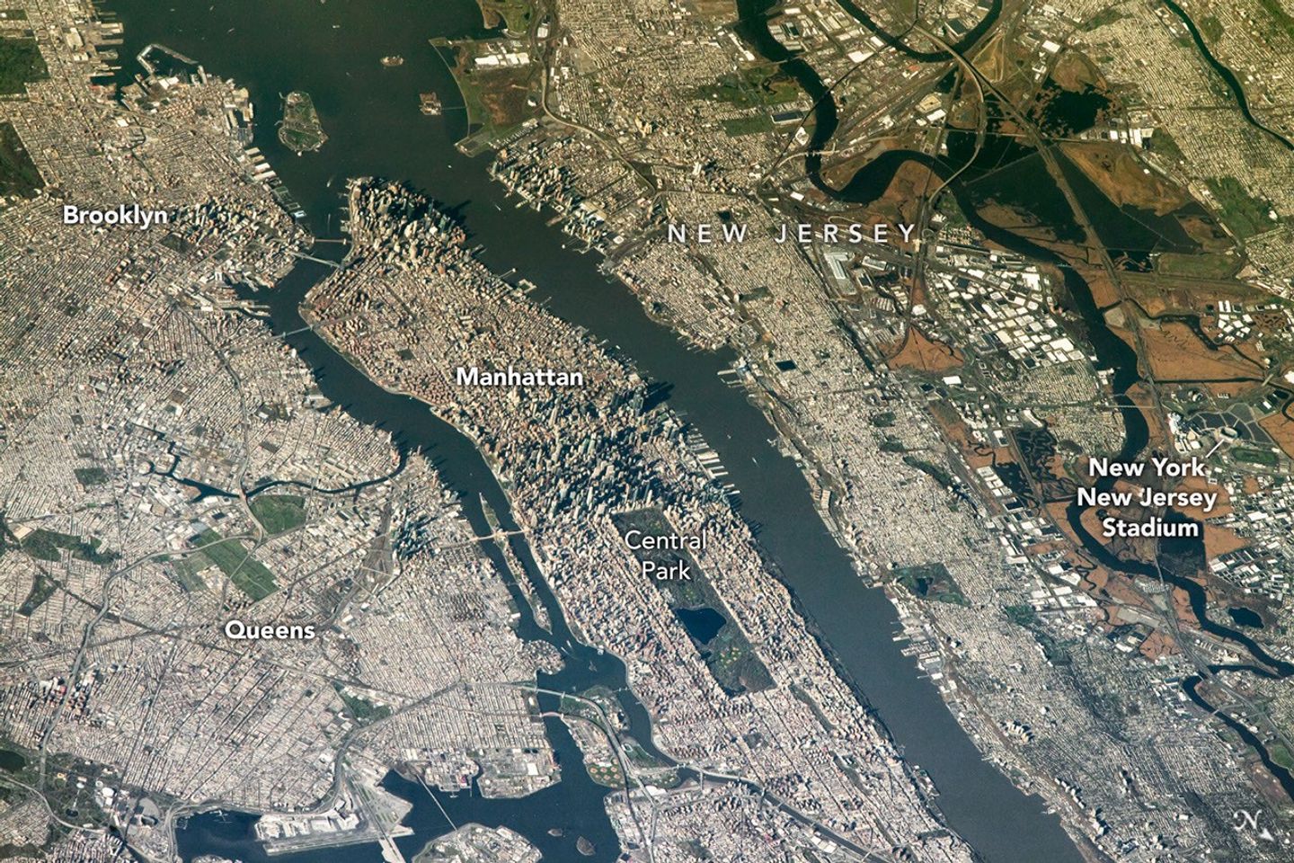 An aerial view of the San Francisco Bay Area Stadium, middle-left, is surrounded by urban infrastructure. Colorful ponds of the southern San Francisco Bay are visible toward the top.