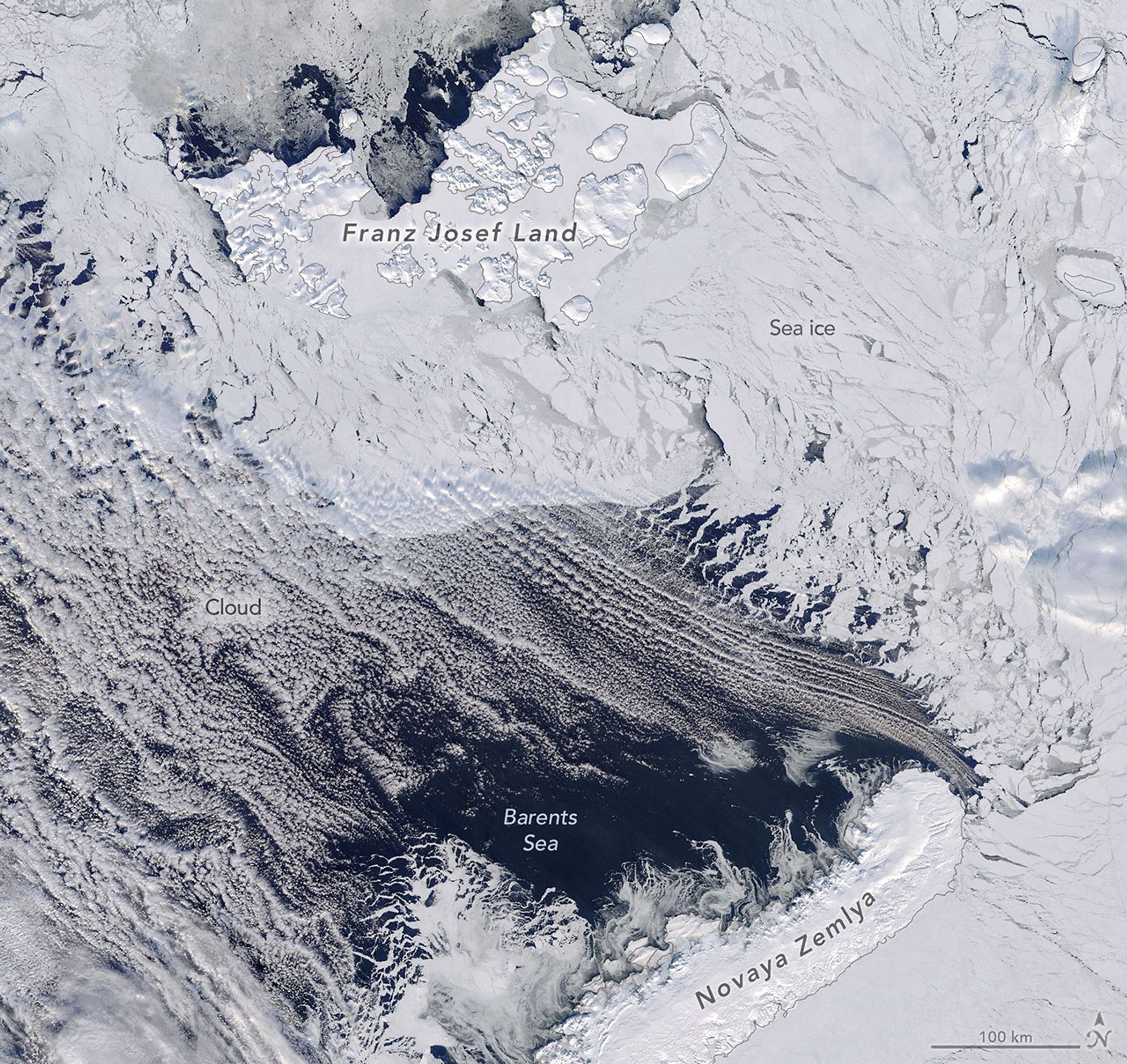 Dark open water lies south of thin, broken up sea ice near Franz Josef Land, with a thin layer of clouds covering part of the scene.