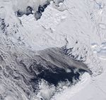 Dark open water lies south of thin, broken up sea ice near Franz Josef Land, with a thin layer of clouds covering part of the scene.