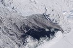Dark open water lies south of thin, broken up sea ice near Franz Josef Land, with a thin layer of clouds covering part of the scene.