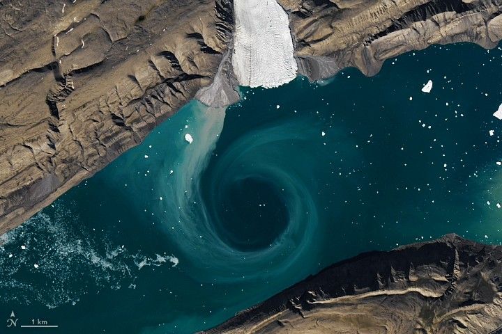 Fjord waters with sediment swirling in a circular eddy, making the water appear light turquoise.
