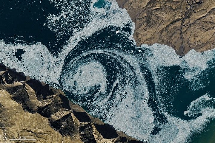 Blue fjord waters with white sea ice swirling in a circular eddy.