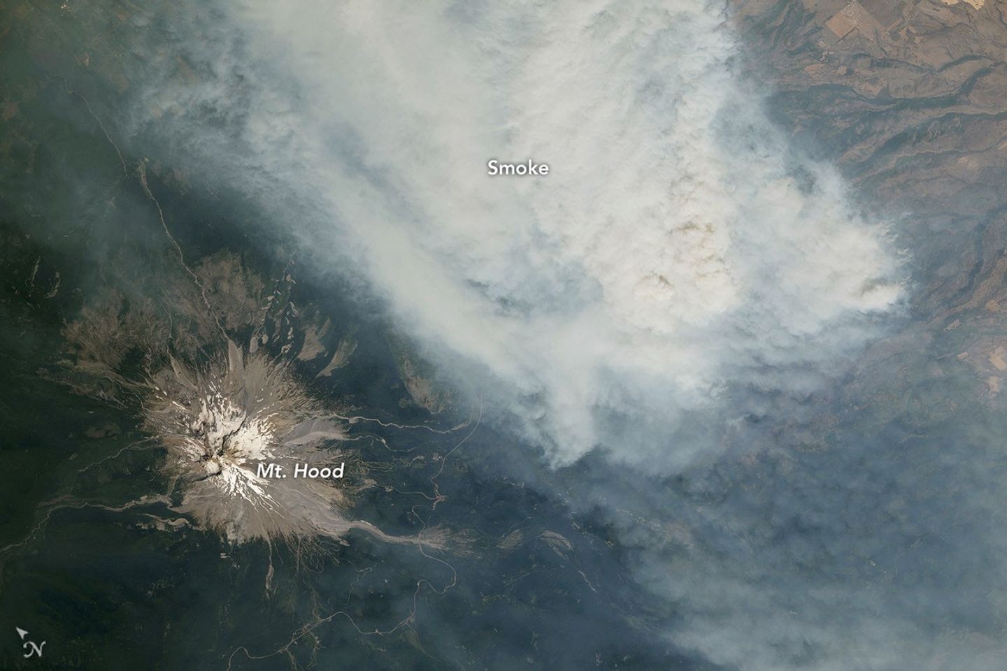 An ice-capped volcano stands at the center of the image, its surrounding terrain blanketed in brown-gray smoke.