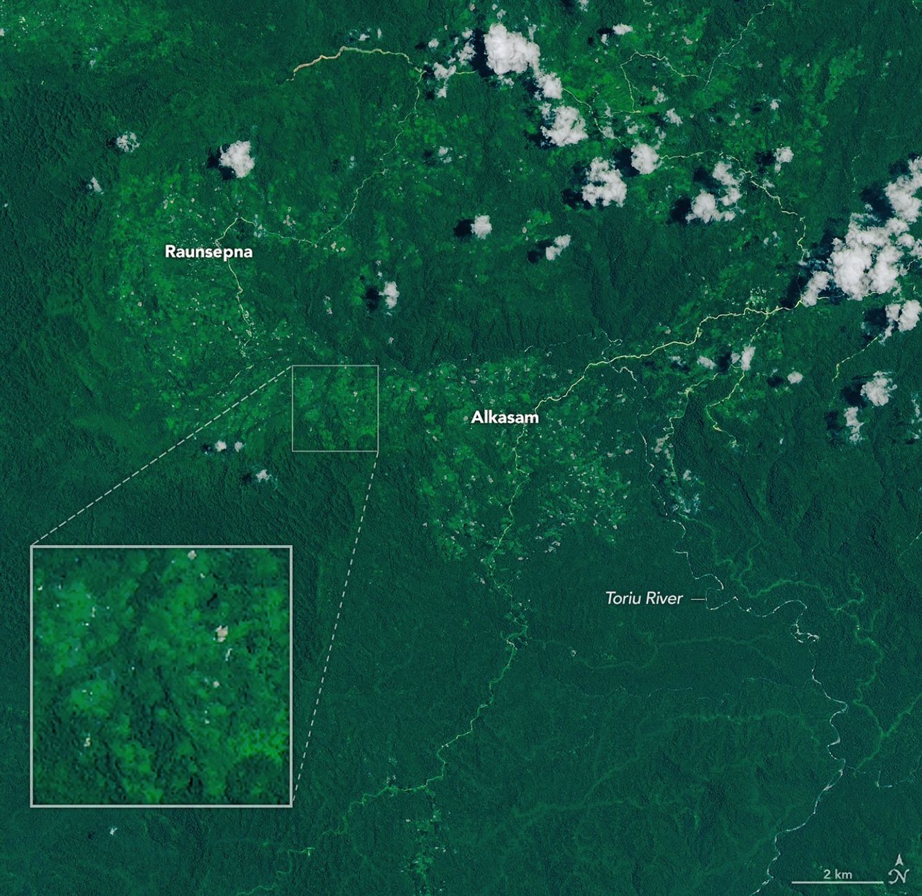A narrow, light-brown landslide scar cuts through dark green forested mountains in East New Britain and extends south toward a stream valley. Rivers swollen with floodwaters, areas of forest clearing, and scattered clouds are also visible in some parts of the image.