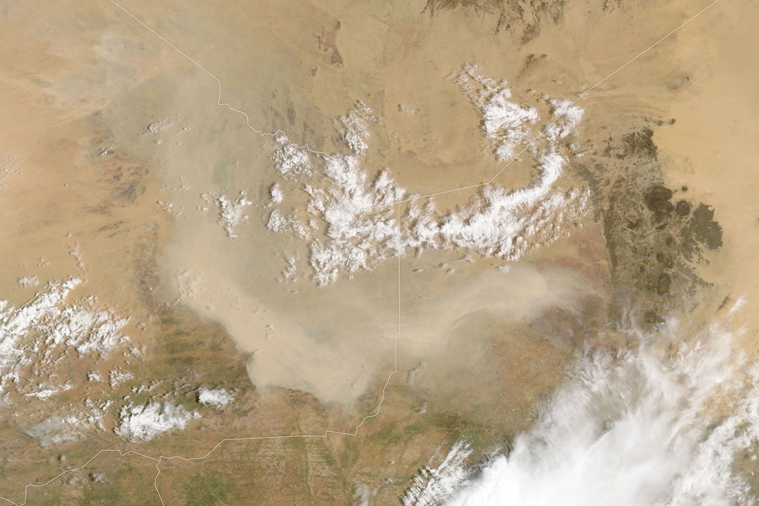 A light brown dust plume, dense at its center and more diffuse toward its edges, extends horizontally across an orange-brown and green landscape. Scattered white clouds cover some of the scene.