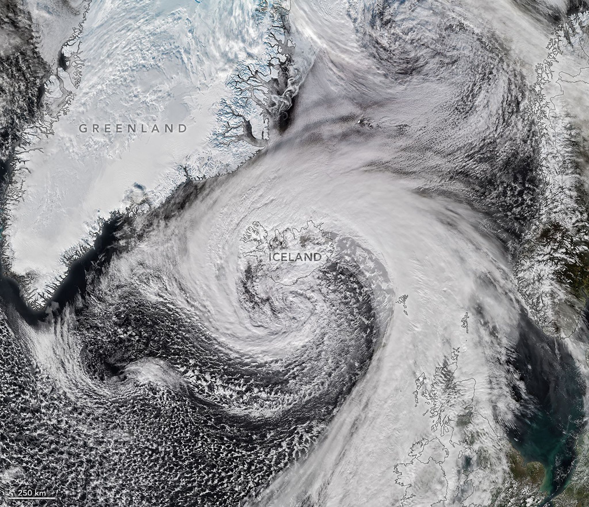 Storm clouds in an expanding spiral are centered near southern Iceland. The system extends across the North Atlantic from Greenland to the UK.