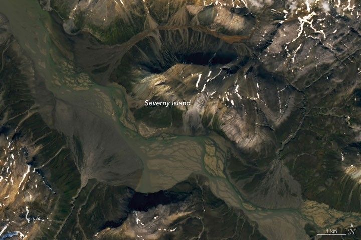 A braided river meanders across the image. Smaller streams empty into the wide channel from either side, forming fan-shaped deposits.