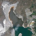 A satellite image of the Great Salt Lake shoreline in 2025 shows exposed gray lakebed with clusters of small dark mounds.