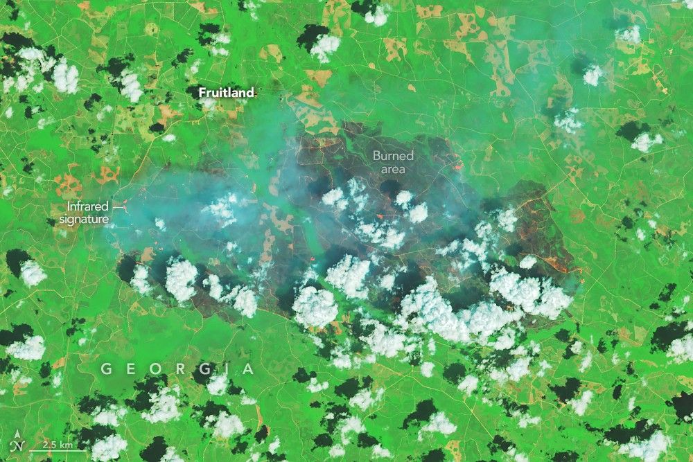 A patch of burned area near Fruitland appears gray amid a background of green vegetation. Small scattered clouds are visible in the lower part of the image.