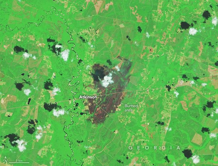 A patch of burned area near Atkinson appears gray amid a background of green. Small scattered clouds are visible in the lower part of the image.