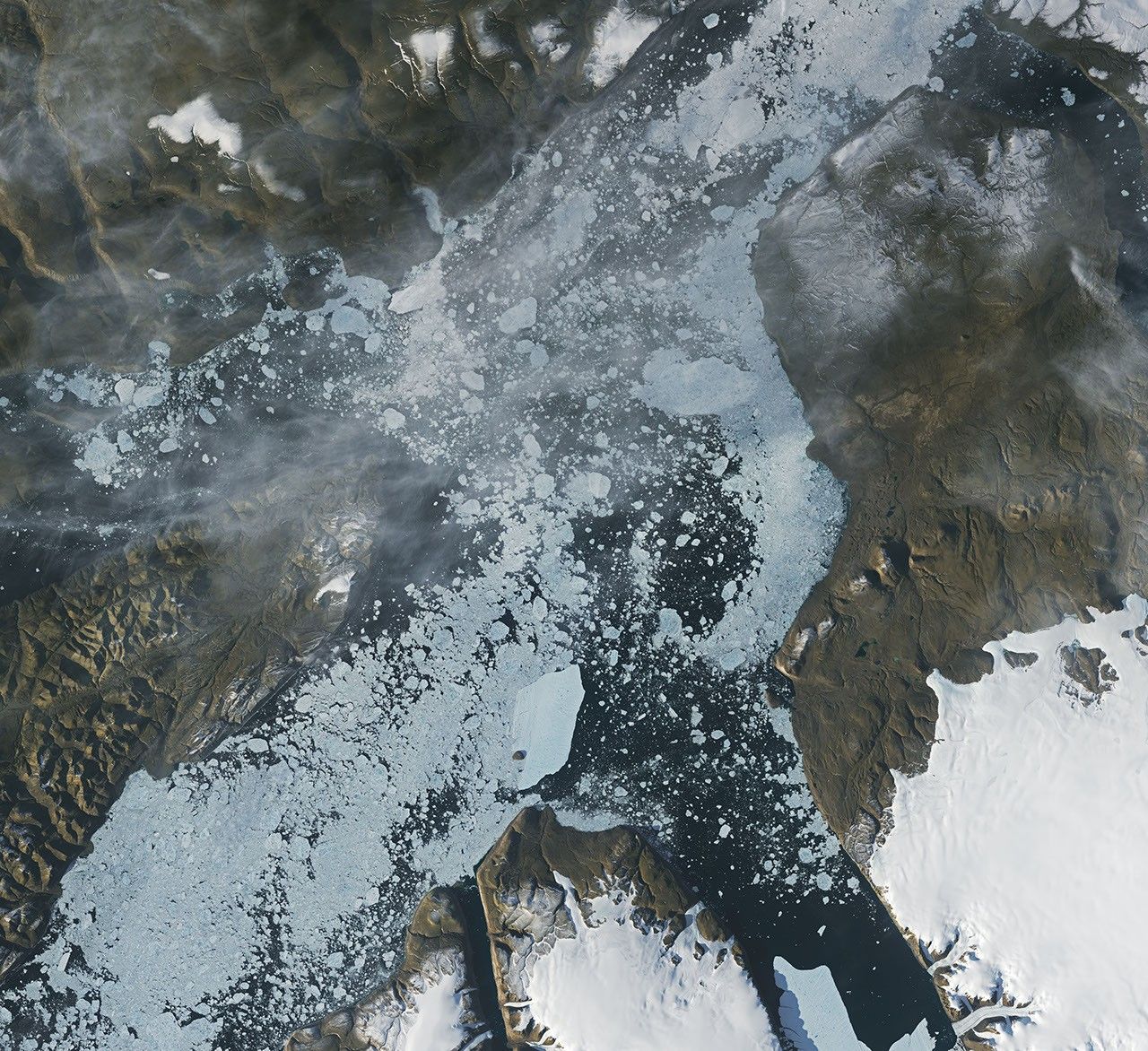 A satellite view shows the iceberg after it pivoted out of the fjord into Nares Strait, wedged against a small, brown island.
