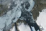 A satellite view shows the iceberg after it pivoted out of the fjord into Nares Strait, wedged against a small, brown island.
