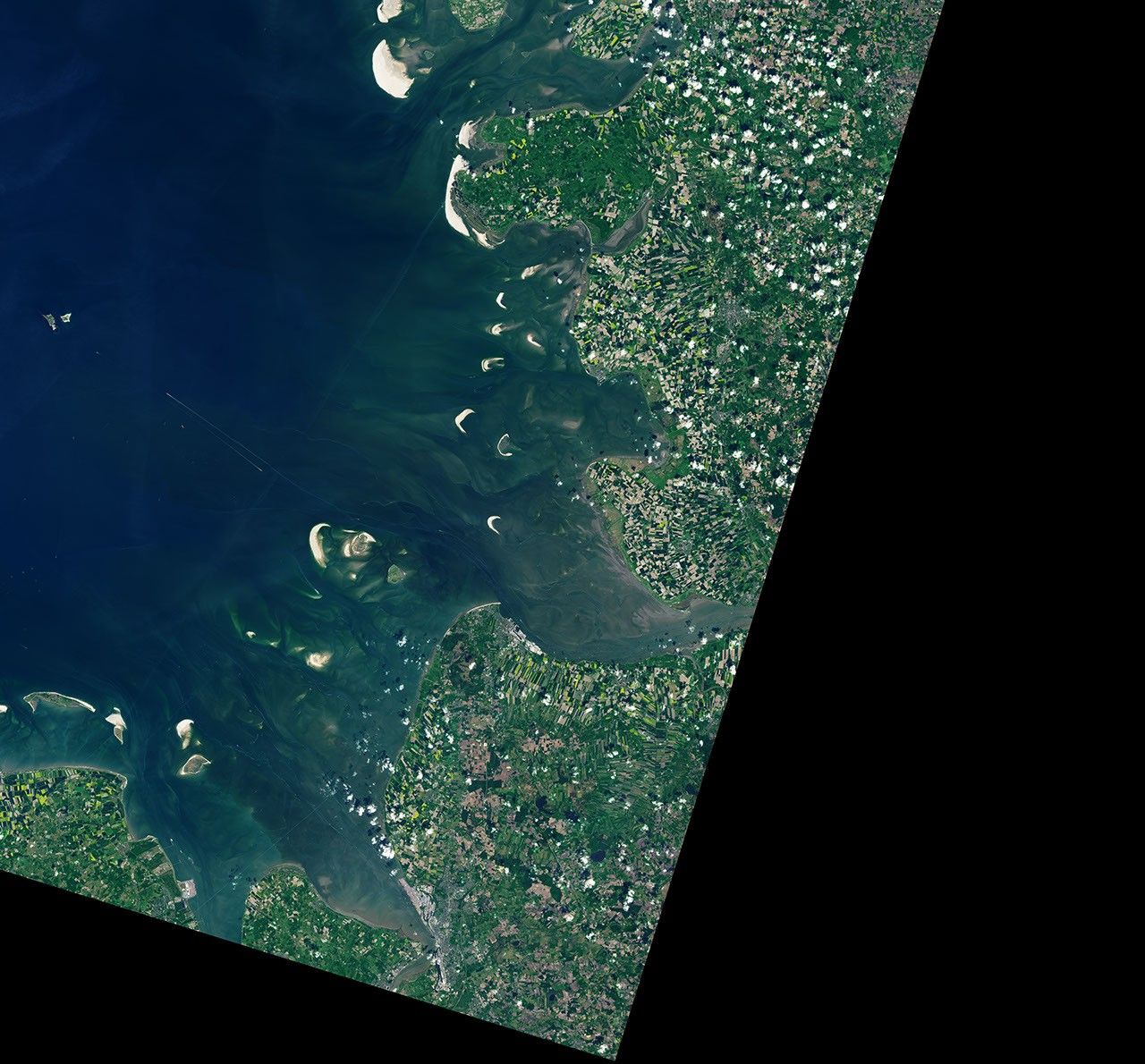 The Elbe river in Germany into the North Sea on the left side of the image. At high tide, a handful of small islands and crescent-shaped sandbars remain exposed above the water level near shore. Ships are visible as small, bright specks on the water.