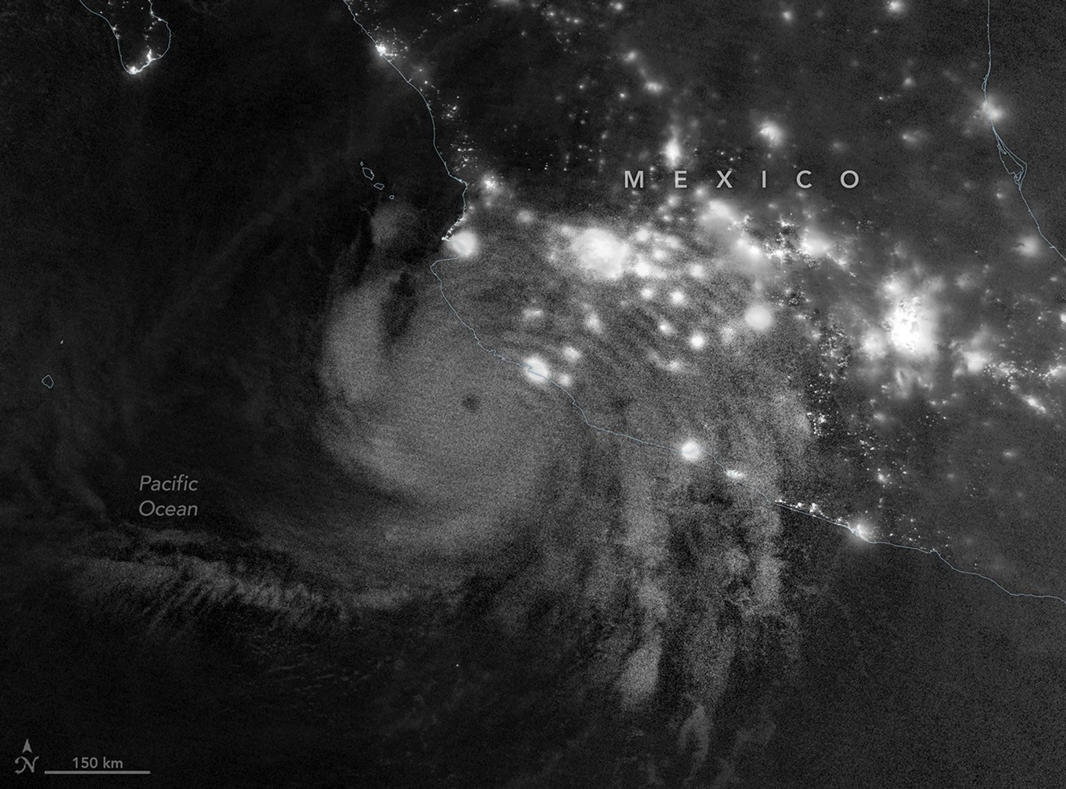 Gravity waves in the upper atmosphere appear as a semicircle of ripples in a nighttime, grayscale satellite image. Hurricane clouds and city lights in Mexico are also visible.
