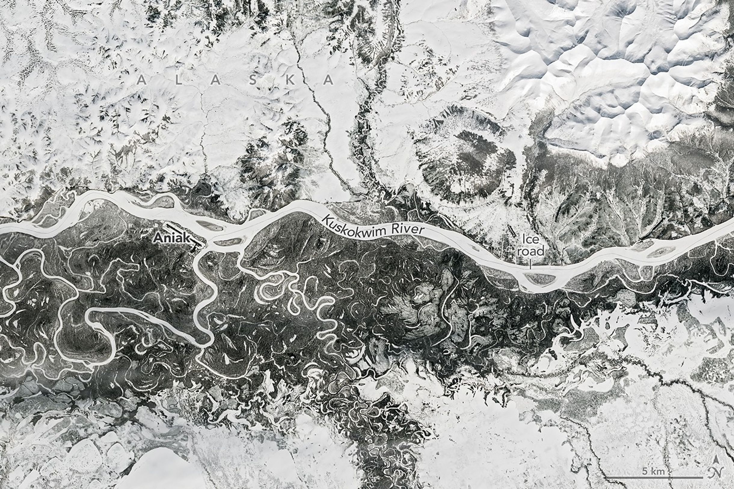 A frozen river winds from east to west past Aniak, Alaska. Nearby meandering channels are also frozen, and much of the surrounding land is snow-covered.