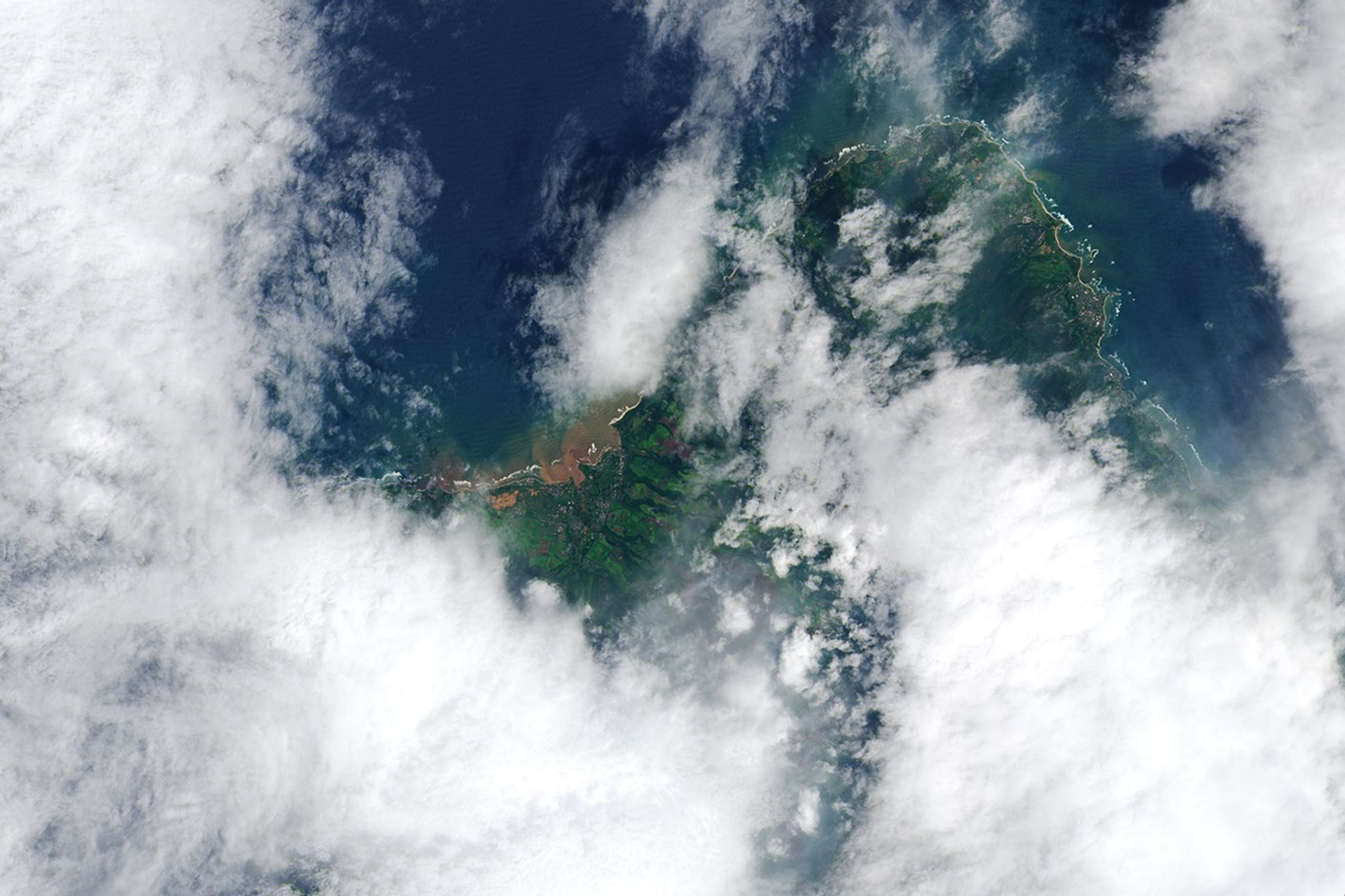 The same area, with brown floodwater pooling across farmland between Mokuleia and Waialua, with a red-brown plume spreading into the coastal ocean.
