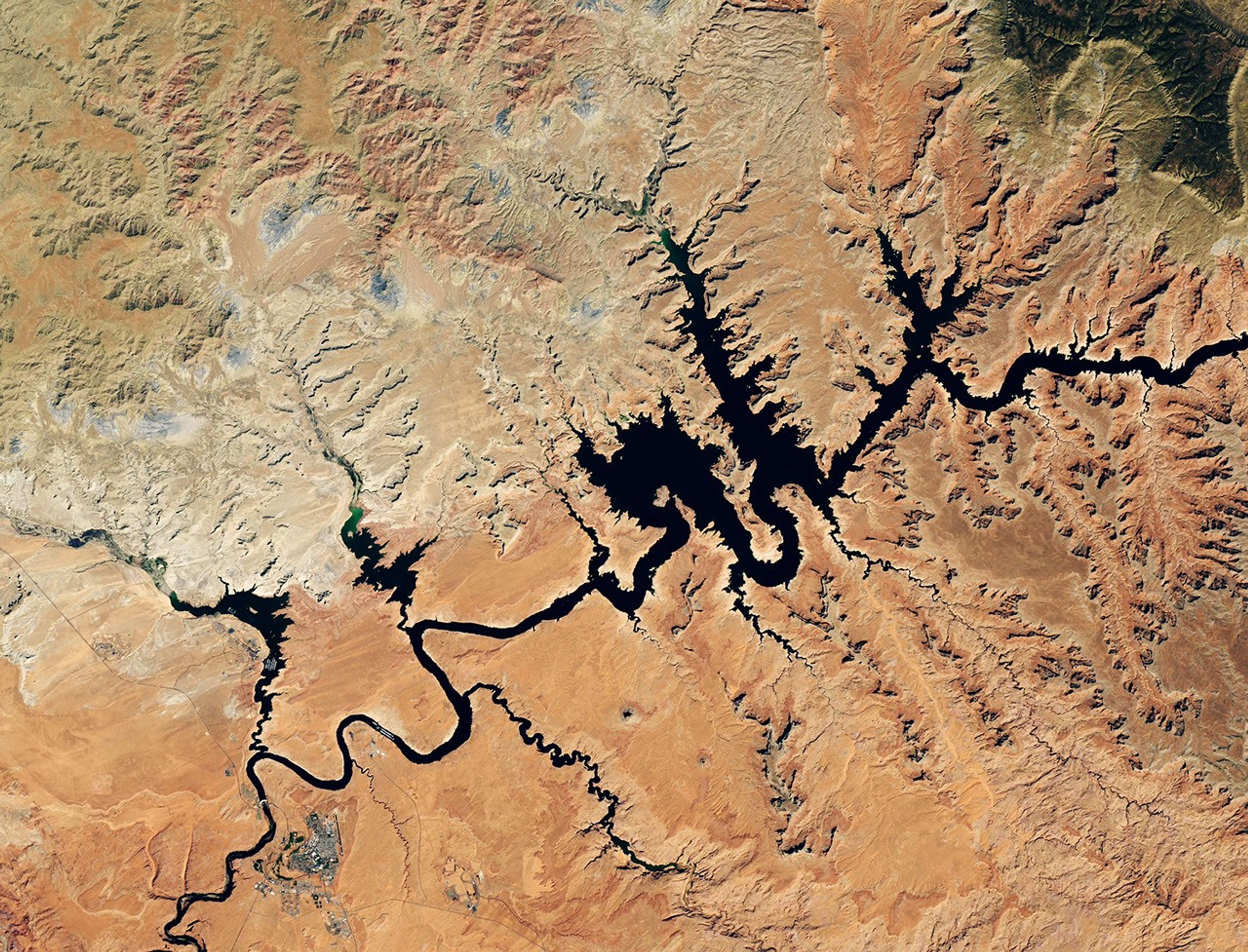 Water in Lake Powell is at record-low levels and looks like a wide river winding through a light orange desert landscape. The Glen Canyon Dam and the town of Page, Arizona, are visible in the lower left.