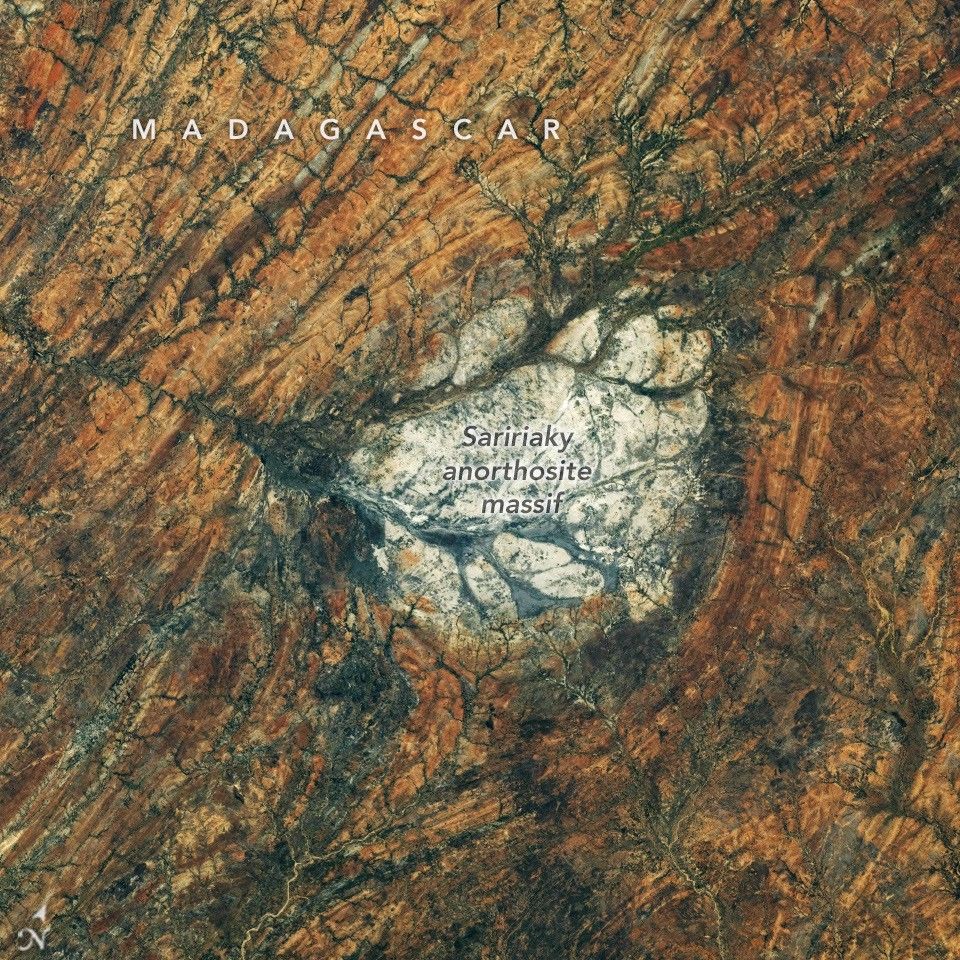 A round, white rock outcrop is surrounded by orange rocks with a north-south linear pattern. Branching riverbeds cut through the rock structures.