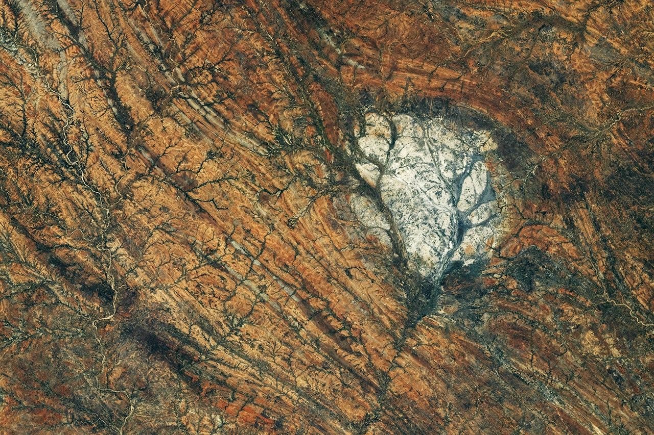 A round, white rock outcrop is surrounded by orange rocks with a north-south linear pattern. Branching riverbeds cut through the rock structures.
