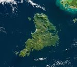 A roughly triangular island is almost entirely covered in green vegetation and has a large inlet on its eastern side.