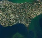 A satellite image from 2015 shows the towns of Leamington and Kingsville along the north shore of Lake Erie in southern Ontario. The surrounding land is divided into rectangular farm fields that appear in shades of green and brown. Light gray and blue greenhouse roofs cover some of the land, mostly between the two towns.