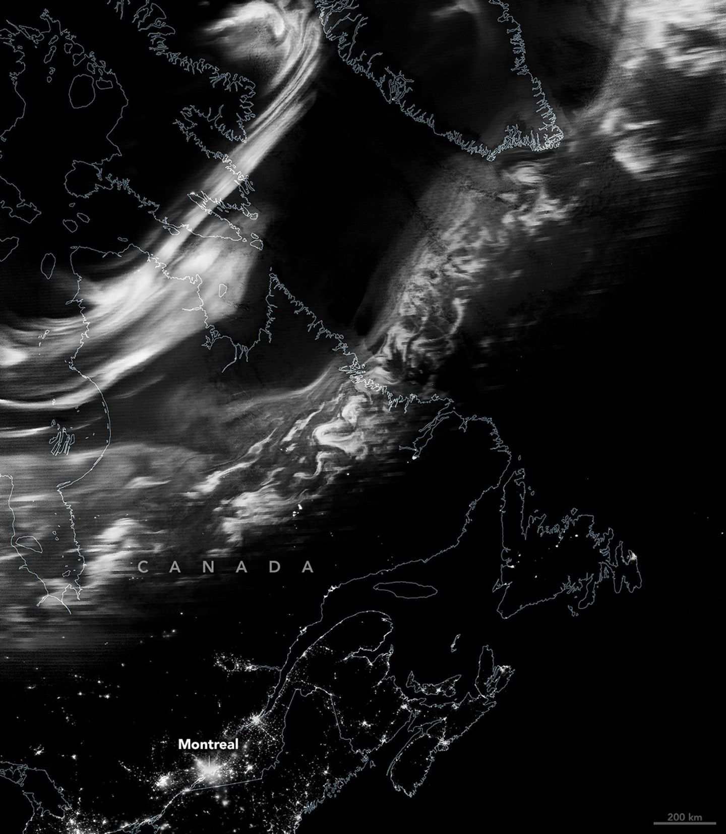 A nighttime satellite image shows a grayscale view of the northern lights stretching from eastern Canada to southern Greenland. Urban light from Montreal and nearby cities appear across the bottom of the scene.