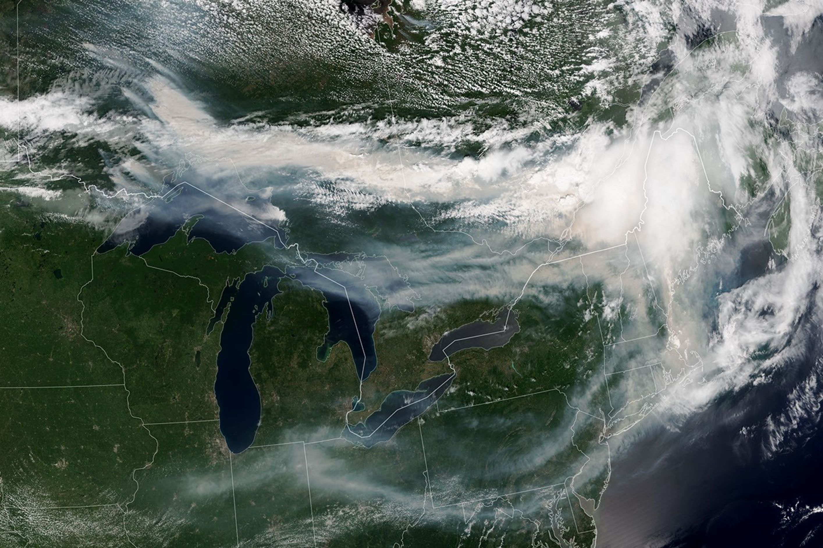 A satellite image shows brown smoke from wildfires in Ontario, Canada, streaming east across parts of Canada and the U.S. Areas of white clouds are mixed in with the smoke.