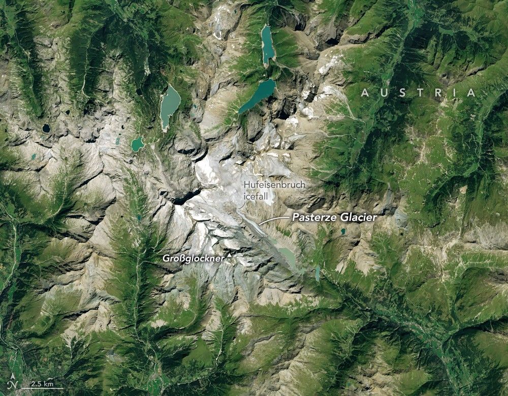 Ice in a broad Alpine basin connects with a short, narrow stretch of glacial ice in the valley below through one small icefall. Lakes fill much of the valley beyond the glacier’s terminus.