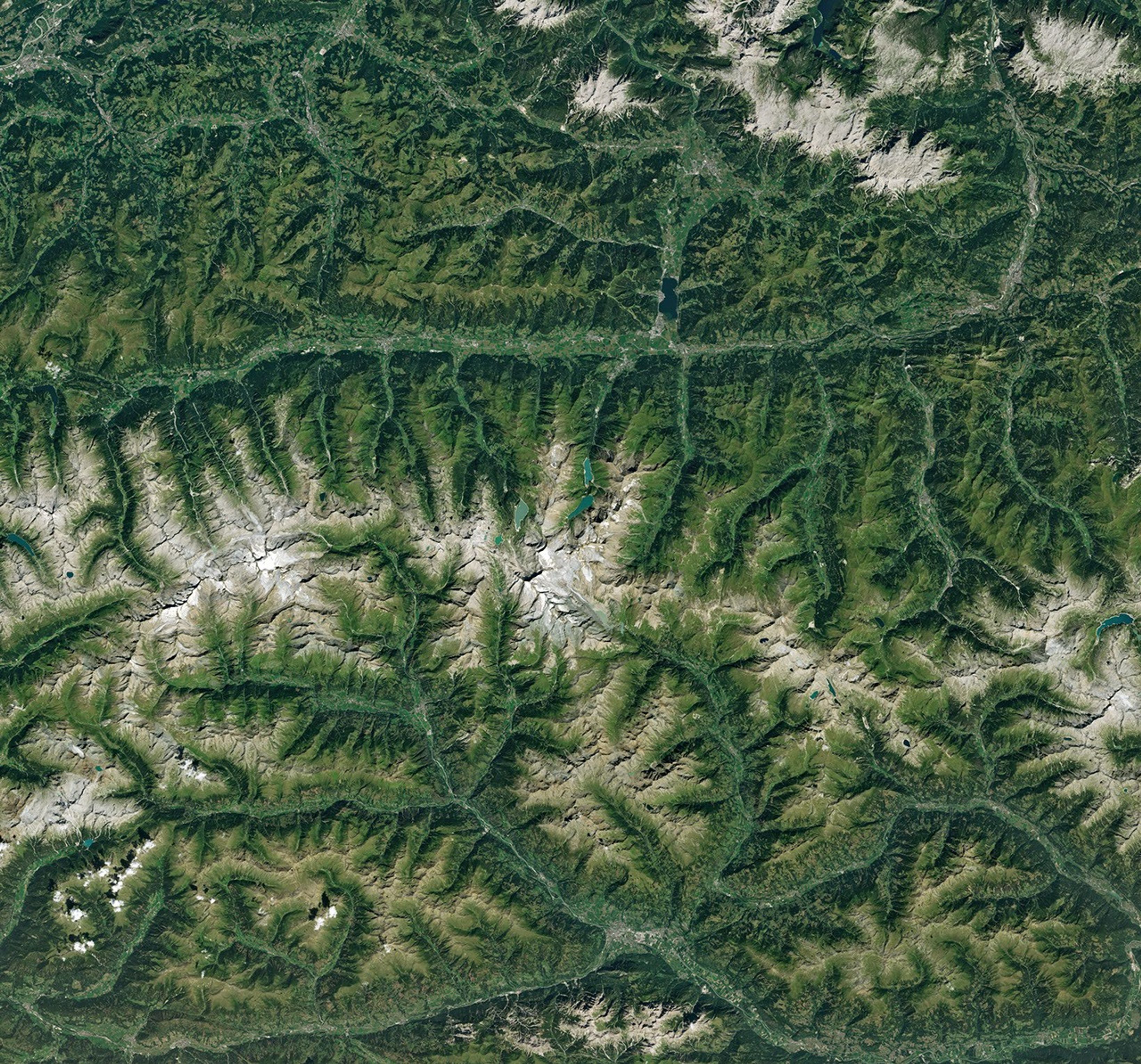 Ice in a broad Alpine basin connects with a short, narrow stretch of glacial ice in the valley below through one small icefall. Lakes fill much of the valley beyond the glacier’s terminus.
