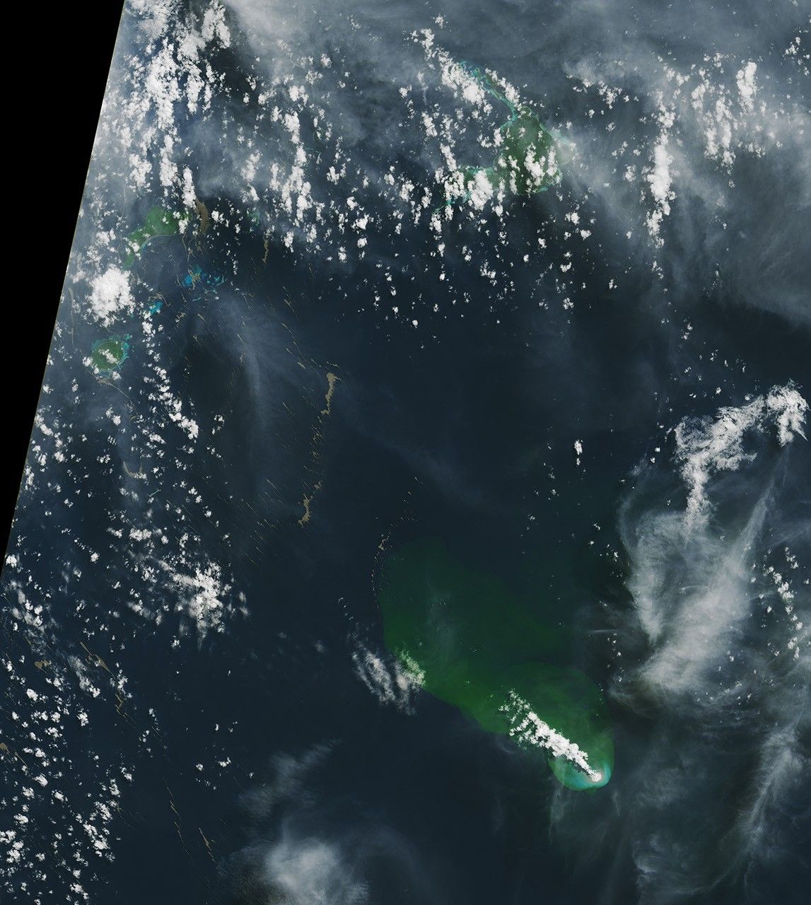 Bands of tan-colored pumice float on the Bismarck Sea near several islands and bright-blue shallow areas. The material lines the southern coast of the largest island. A bright-white volcanic plume and an area of greenish water extend to the northwest from an underwater eruption.