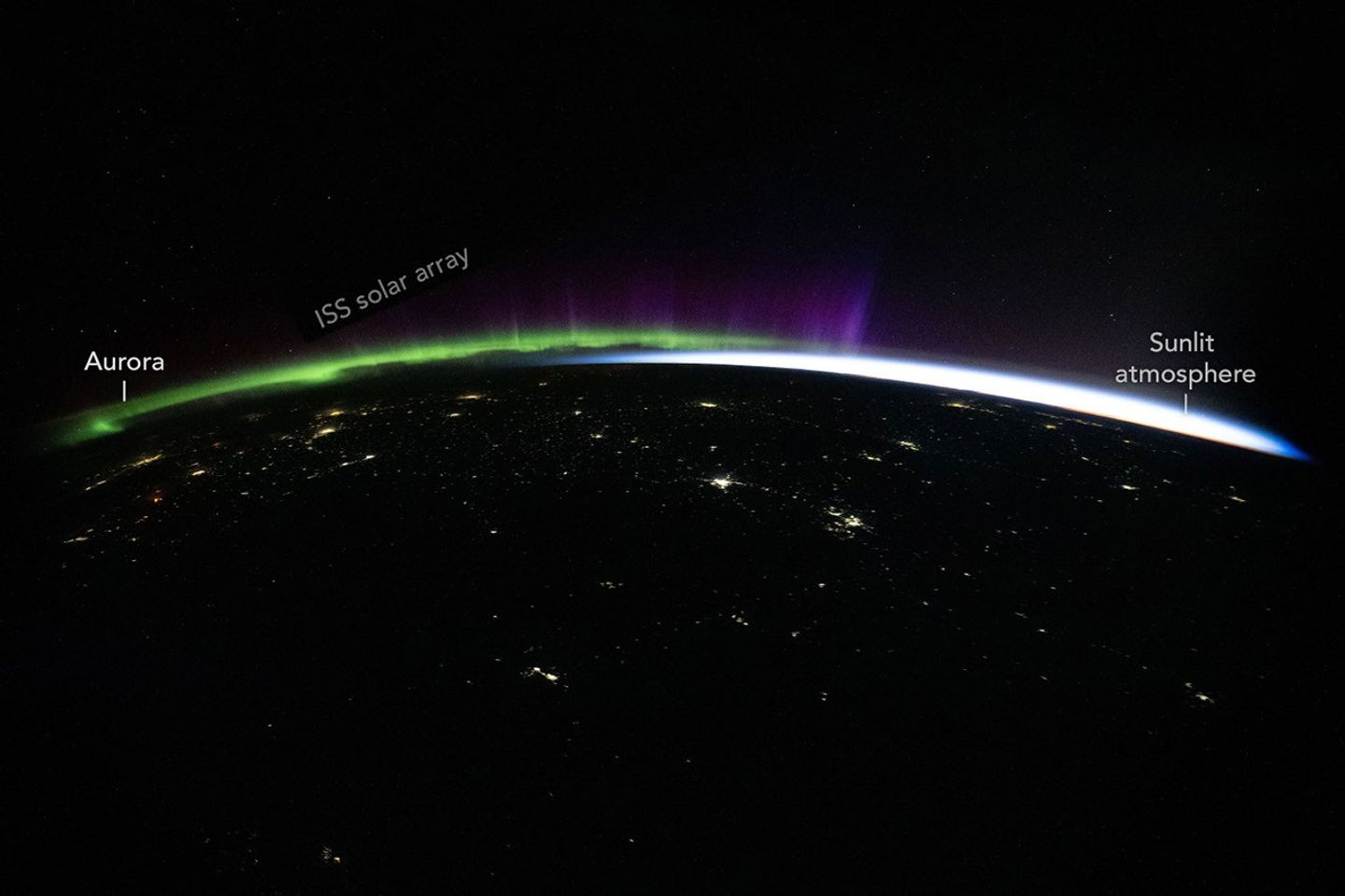 Green and purple aurora and white airglow arc above Earth’s limb and the scattered city lights of Central Asia in a nighttime photo taken from the International Space Station.
