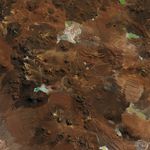 A plateau in the Chilean Andes is surrounded by stratovolcanoes and lava domes. The dry, mostly brown landscape has a lighter brown patch near the center, marking the radio telescope array.