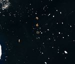 Several small islands, their surfaces tinged pink-orange, dot a dark ocean scattered with drifting sea ice.