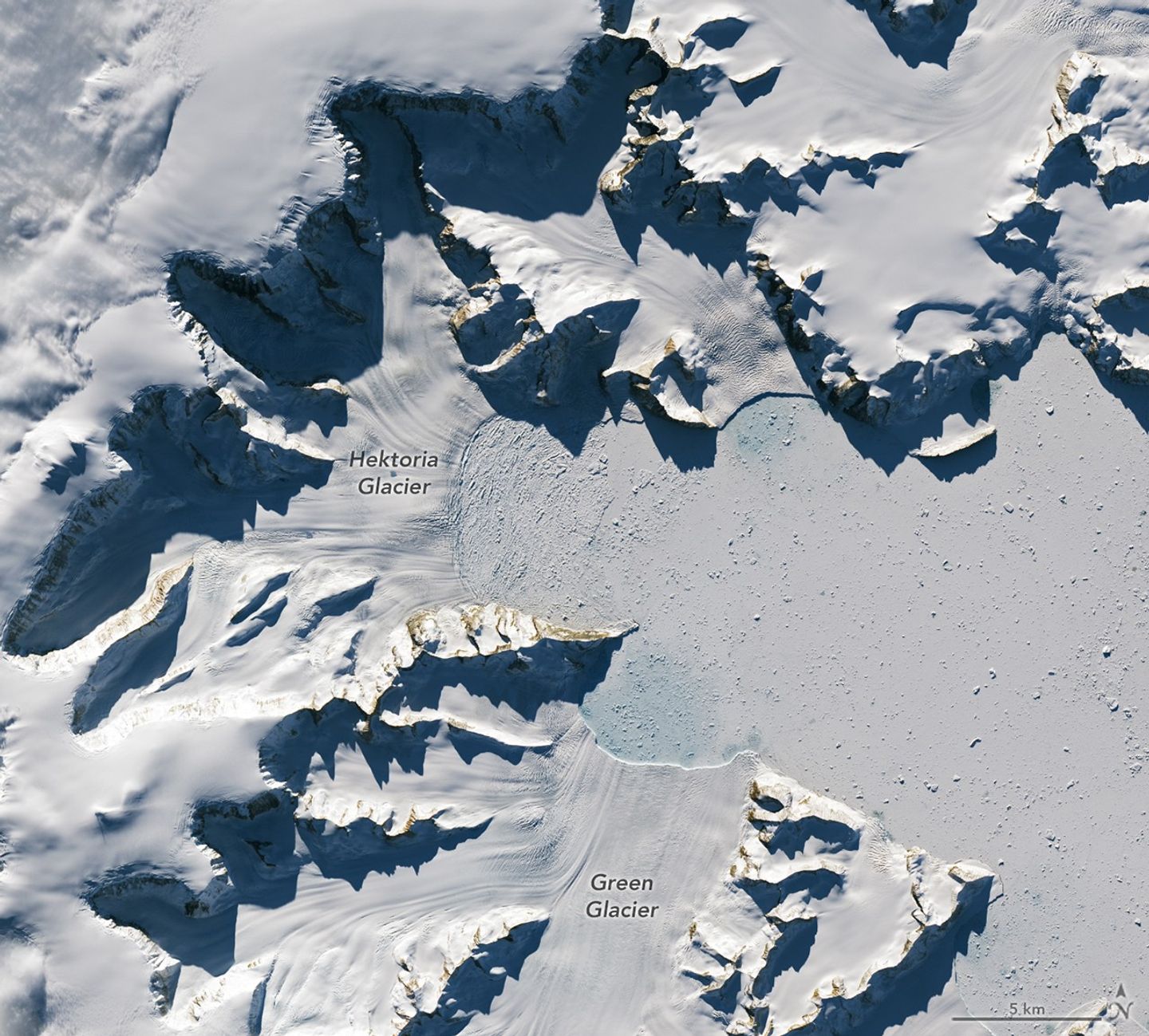 Glaciers flow from the left and bottom sides of the image, terminating much closer to the cliffs than in the previous image.